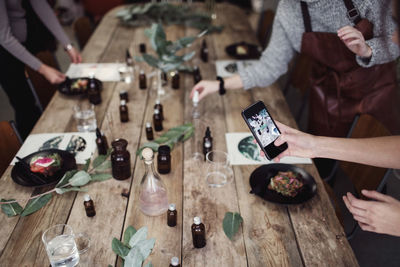 Cropped hand of woman photographing table by female colleague standing at perfume workshop