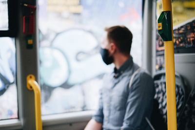 Defocused image of man wearing mask looking away while sitting in bus