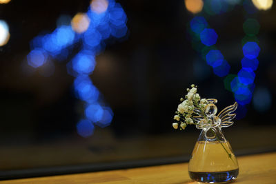 Close-up of flower vase illuminated on table against defocused lights