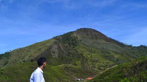 Rear view of man looking at mountain against blue sky