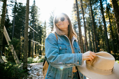 Young woman wearing sunglasses standing by trees in forest