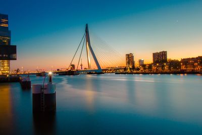 Illuminated city by river against sky during sunset