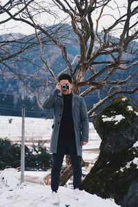 Man with camera standing on snow against trees