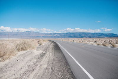 Empty road by landscape against blue sky