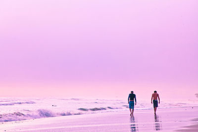 Rear view of men walking at beach during sunset