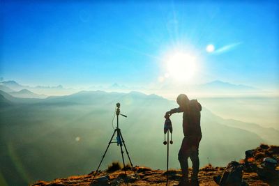 Man standing by tripod on mountain during sunny day