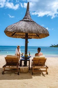 People sitting on lounge chairs at beach against sky