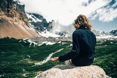 Rear view of woman sitting on rock looking at mountain