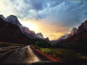 Road by mountains against sky during sunset