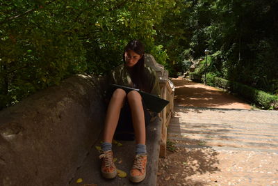 Woman reading book while sitting against trees