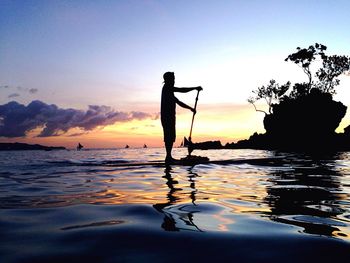 Silhouette man paddleboarding on sea during sunset