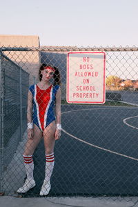 Full length portrait of woman in sports clothing seen through chainlink fence with sign