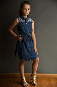 Full length portrait of girl with hand on hip standing against wall