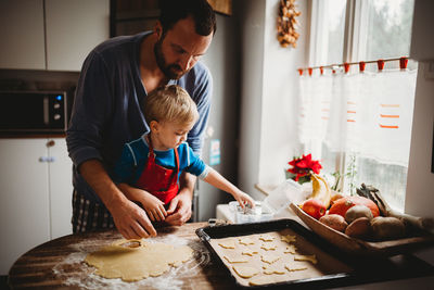 Father and son in kitchen at home baking christmas cookies in pajamas