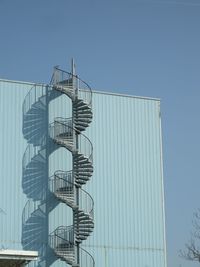 Low angle view of metallic spiral staircase by wall against clear sky