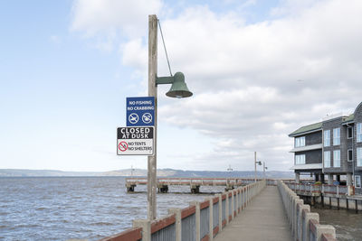 Road sign by sea against sky