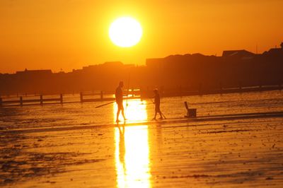 Silhouette people on beach against sky during sunset