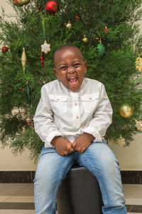 Portrait of cheerful boy sitting on christmas tree