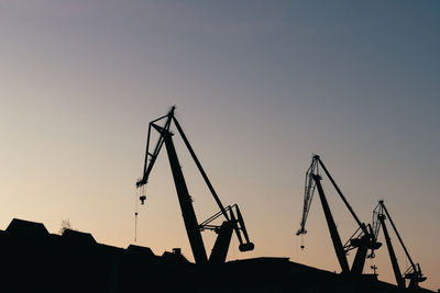 Low angle view of silhouette cranes against clear sky at sunset
