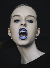 Close-up portrait of young woman against black background 