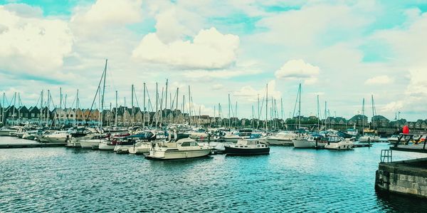 Sailboats moored on harbor against sky in city