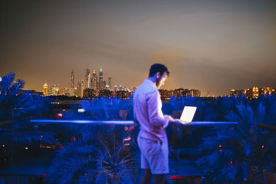 Full length of man standing by illuminated buildings against sky at night