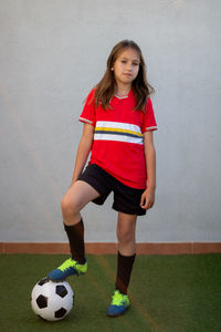 Portrait of smiling girl with soccer standing against wall