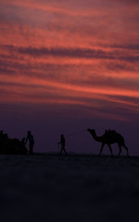 Silhouette people on land against sky during sunset