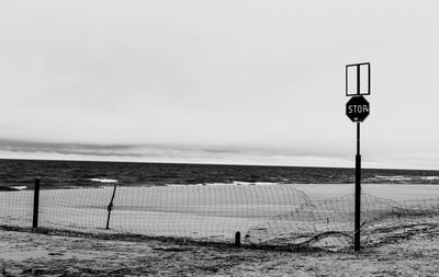 Stop sign and fence by water against sky