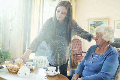 Young woman serving breakfast to grandmother at home