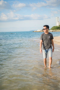 Full length of young man standing at beach against sky