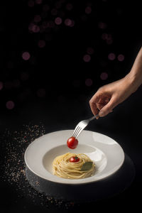 Plate with spaghetti and cherry tomatoes in fork held by female