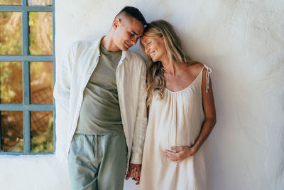 Couple in love standing near the wall. a pregnant woman holds her husband's hand.