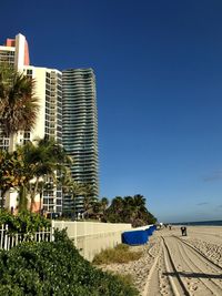 Modern buildings by sea against clear blue sky