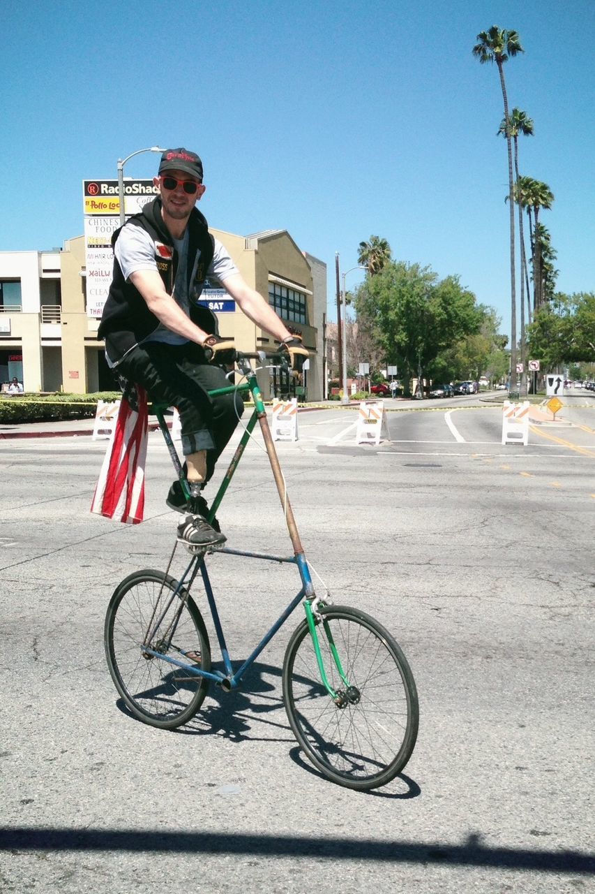 bicycle, transportation, mode of transport, land vehicle, building exterior, architecture, built structure, clear sky, riding, street, full length, lifestyles, city, leisure activity, stationary, cycling, blue, sunlight