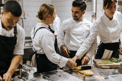Young female chef talking with male colleague while standing near kitchen counter at restaurant