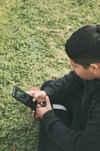 Top view young boy sitting in the park, looking at his smart phone, selective focus