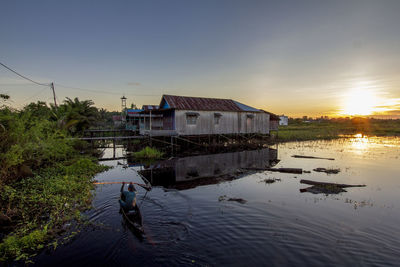Houses by lake and buildings against sky during sunset
