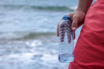 Close-up of man holding plastic bottle against sea