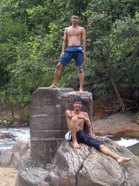 Portrait of friends on rock by stream at forest