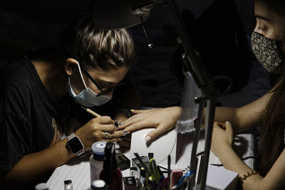 Female stylist in mask making manicure to woman during covid epidemic