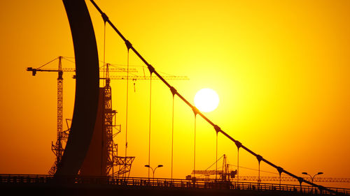 Silhouette cranes at construction site against orange sky