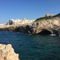 Buildings by sea against clear blue sky