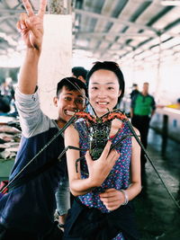 Portrait of smiling friends holding sea animal while standing at market