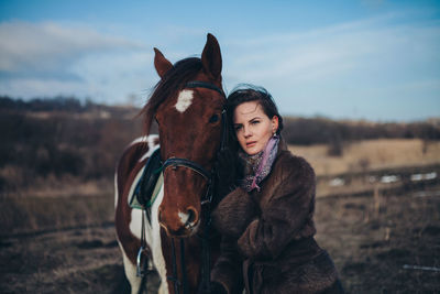 Beautiful young woman with horse standing on field