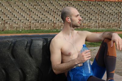 Shirtless man listening music while sitting on field