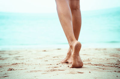 Low section of woman walking at sandy beach