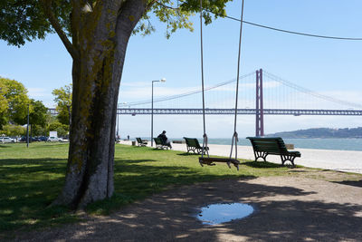 People on bench by bridge against sky
