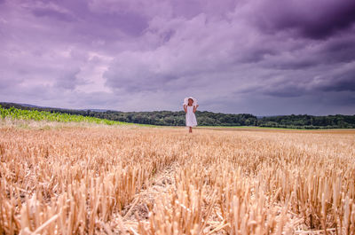 Girl standing amidst agricultural field against cloudy sky