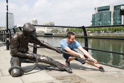 Smiling young man pulling rope of statue by river